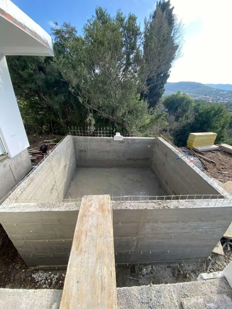 Concrete swimming pool basin under construction with trees and hills behind