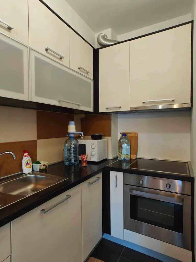 Compact kitchen corner with cream cabinets, black countertop, and oven