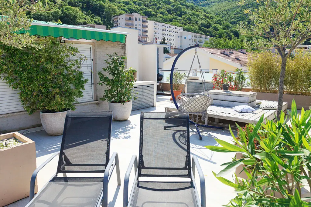 Rooftop terrace with lounge chairs, potted plants, and hanging chair