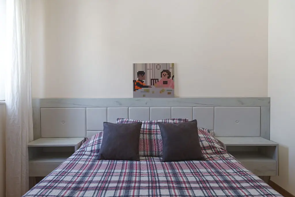 Bed with plaid bedding, dark pillows, and pixel art above headboard