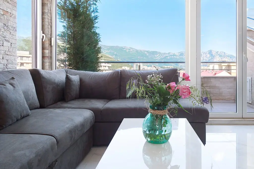 Gray sectional sofa and vase of flowers by mountain view window