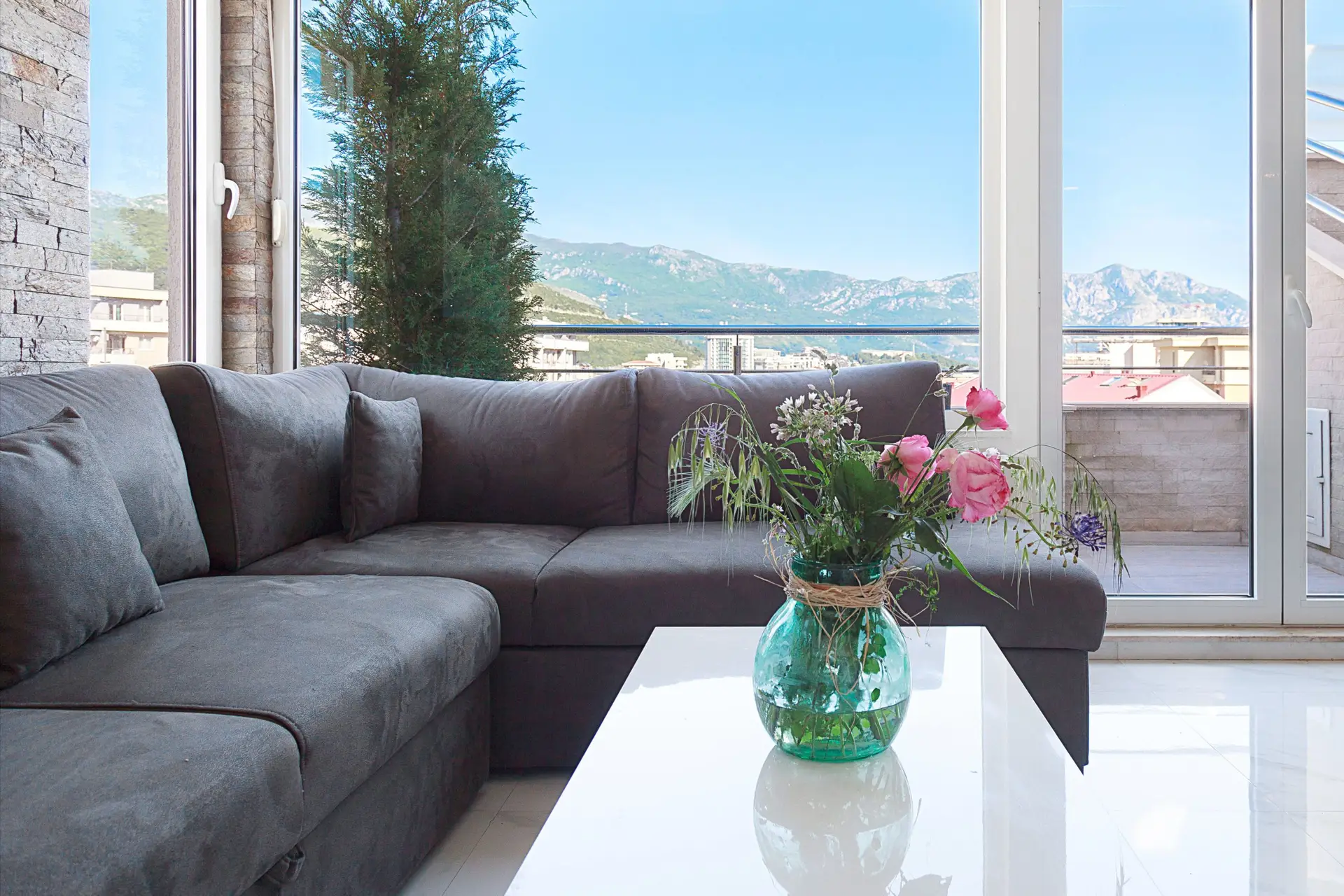 Gray sectional sofa and vase of flowers by mountain view window