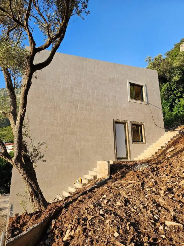 Unfinished beige house with exterior stairs and tree under blue sky
