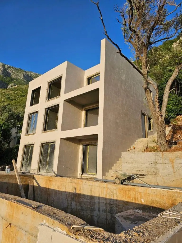 Three-story beige house under construction on a hillside