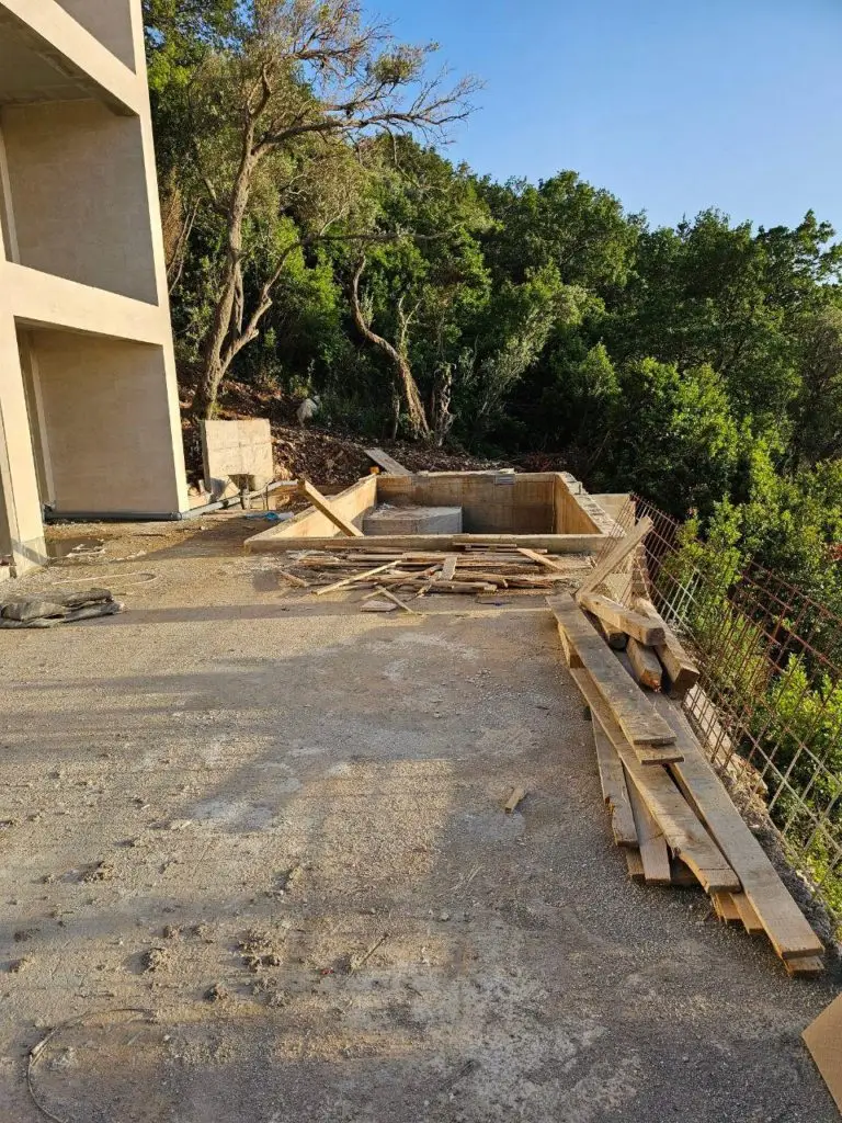 Construction site beside building with stacked wooden planks and trees