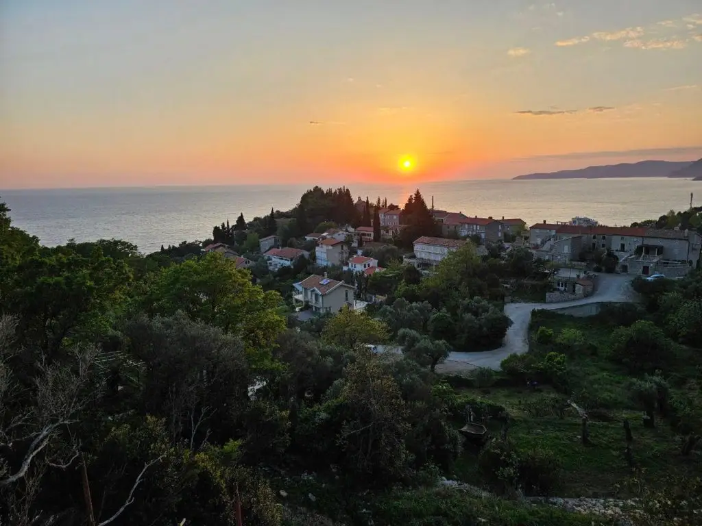 Sunset over coastal village and sea with distant hills