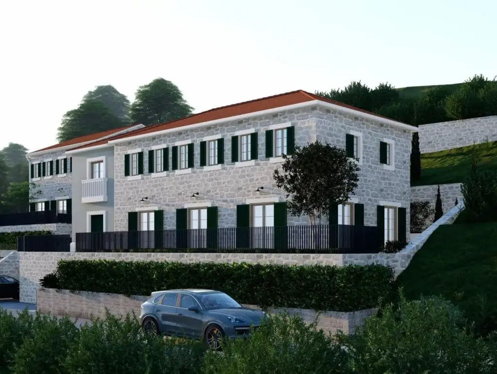 Stone house with green shutters on a hillside, with parked car
