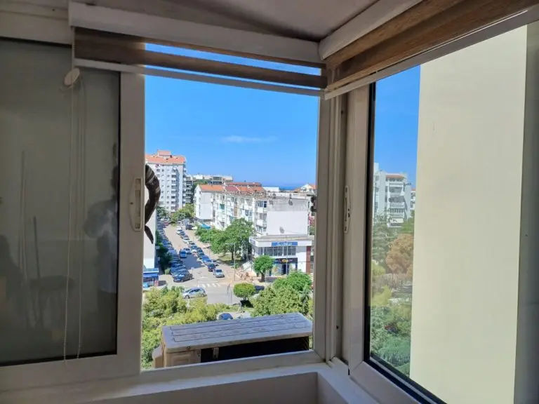 View through an open window of a city street with buildings and trees