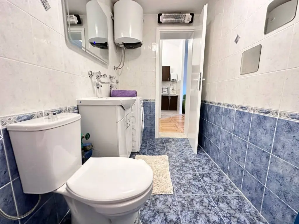Blue-tiled bathroom with toilet, sink, and washing machine