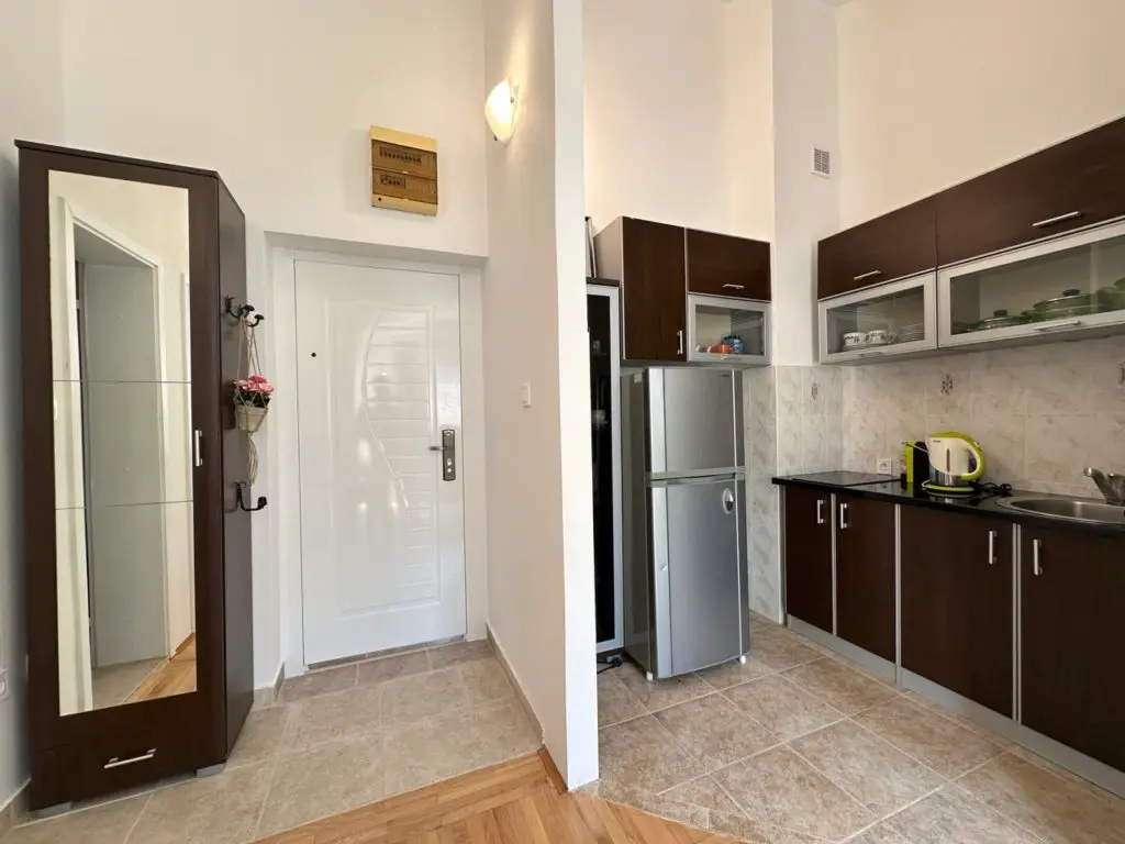 Hallway leading to a compact kitchen with brown cabinets and refrigerator