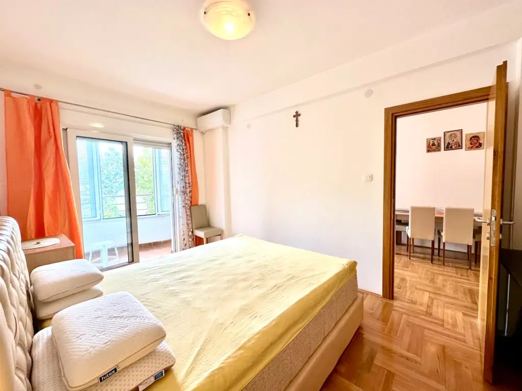 Bright bedroom with bed, orange curtains, and balcony door