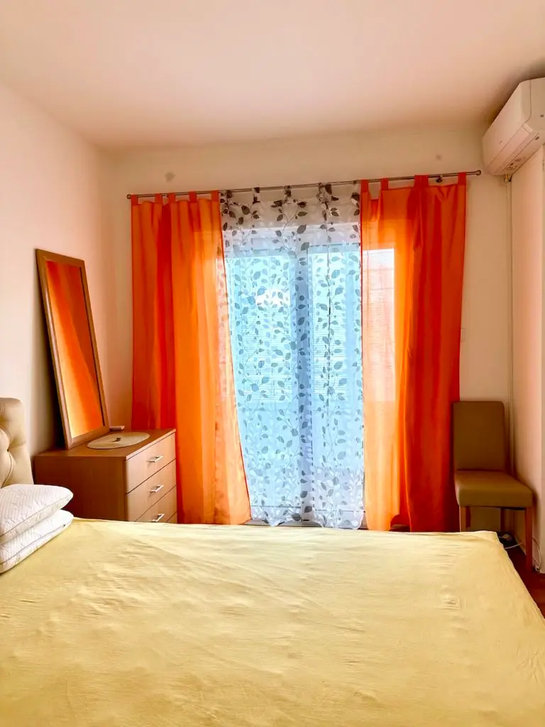 Bedroom with bed, dresser, mirror, and orange curtains