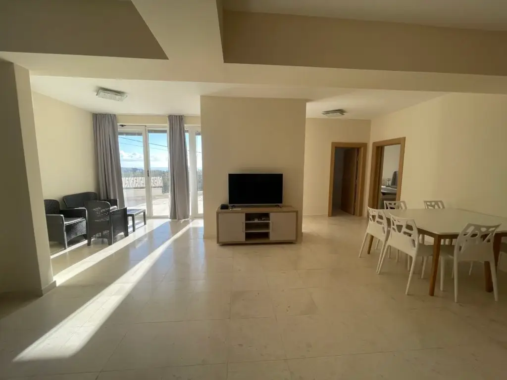Spacious living room with TV, dining table, and balcony doors