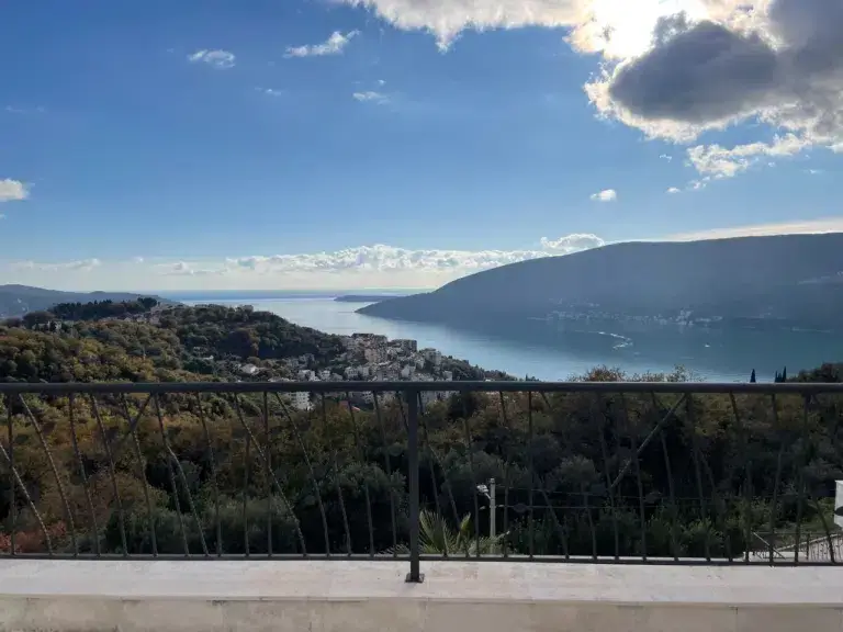 Balcony railing overlooking a bay and hillside under cloudy sky