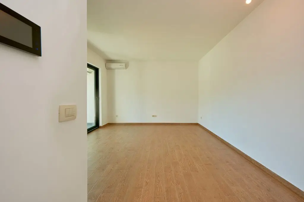 Empty unfurnished room with wood floor, white walls, balcony door, and air conditioner