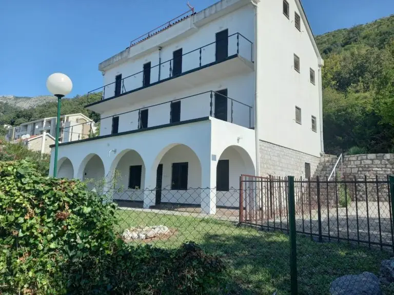 White three-story house with arches, balconies, and fenced yard