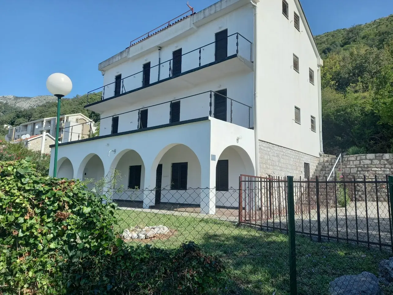 White three-story house with arches, balconies, and fenced yard