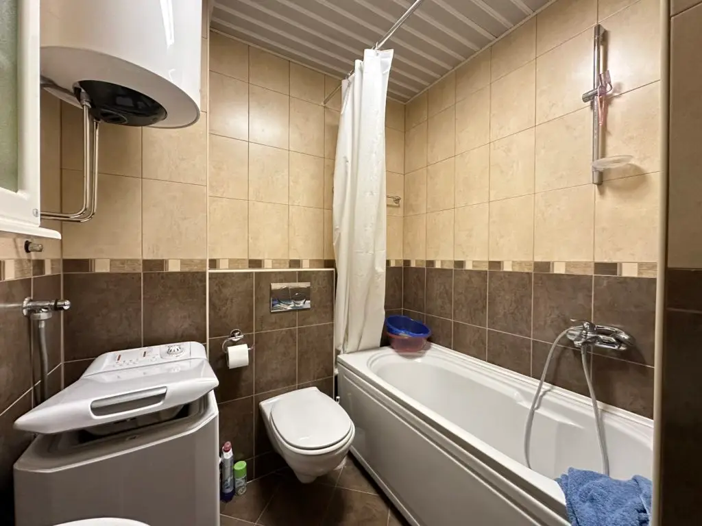 Compact bathroom with bathtub, toilet, and washing machine