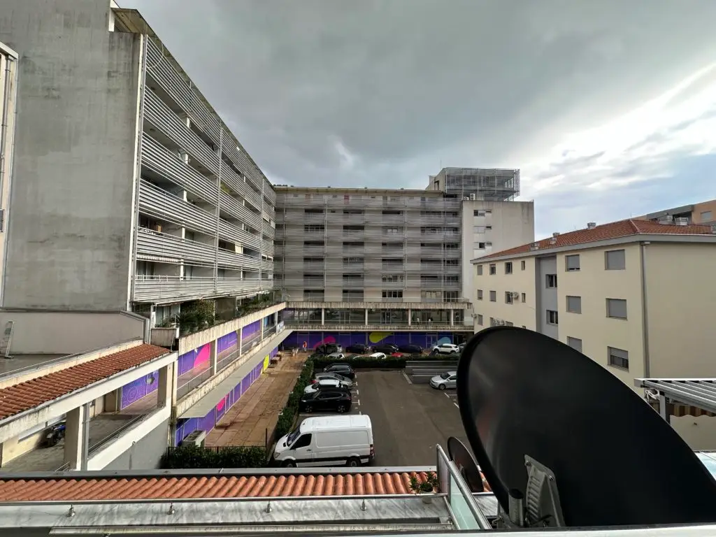 Balcony view of apartment buildings and parking lot, with satellite dish
