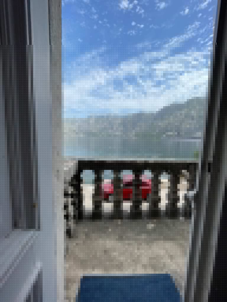 Doorway view of stone balcony, red car, bay, and mountains