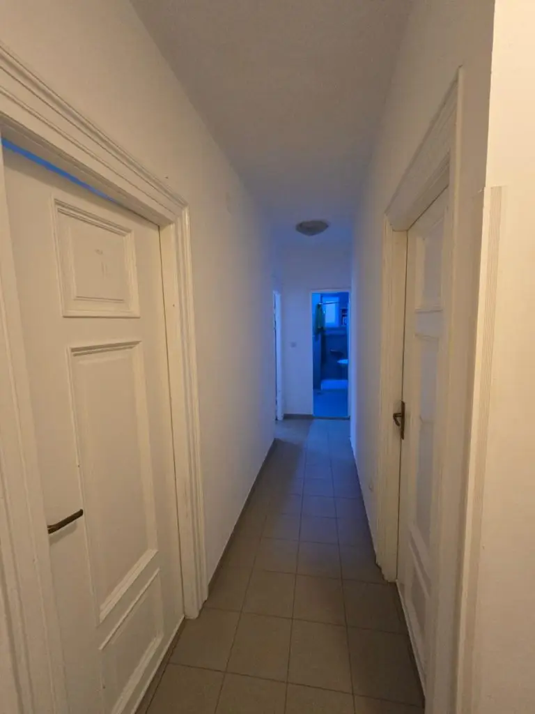 Narrow white hallway with tiled floor and doors on both sides