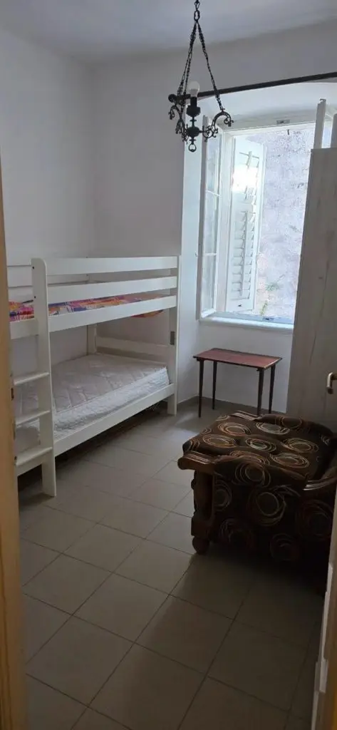 Small room with white bunk bed, window, and patterned ottoman