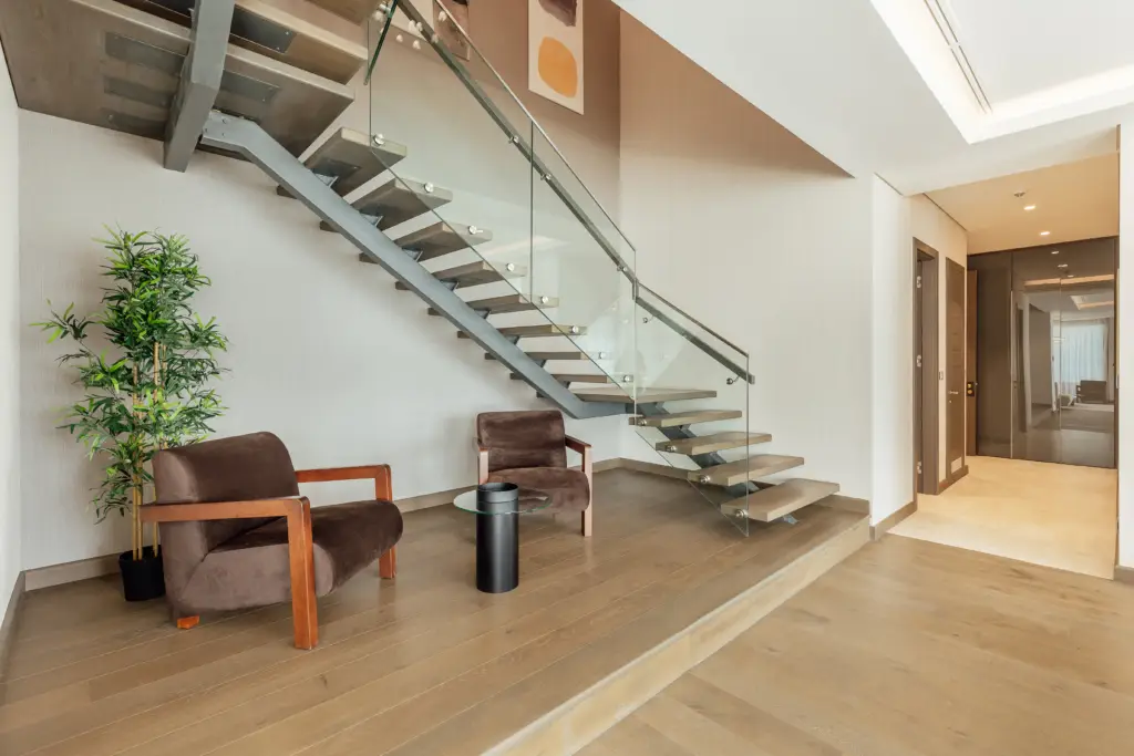 Modern interior with floating staircase, brown chairs, and potted plant