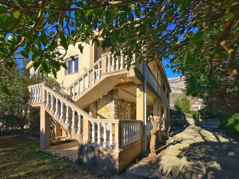 Beige house with exterior staircase and balcony in a leafy yard