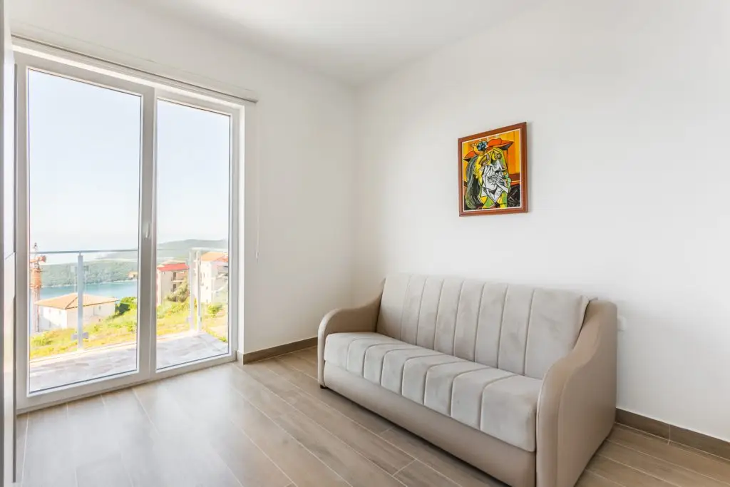 Bright room with beige sofa, wall art, and sea view through doors