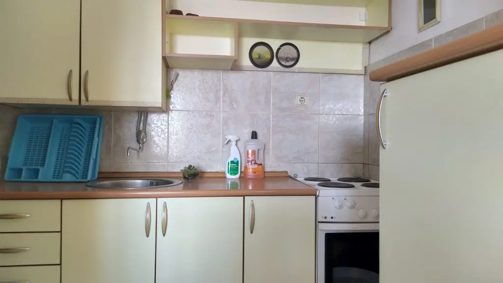 Compact kitchen with beige cabinets, sink, stove, and dish rack