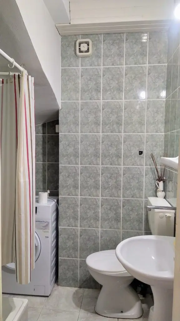 Small tiled bathroom with shower curtain, toilet, sink, and washing machine