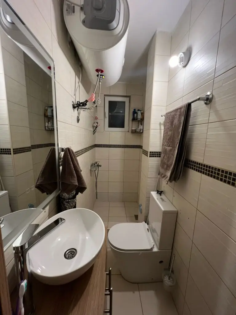 Narrow tiled bathroom with sink, toilet, shower, and towels
