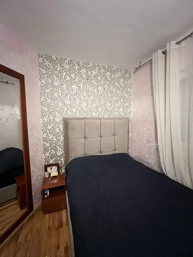 Small bedroom with bed, patterned accent wall, mirror, and curtains