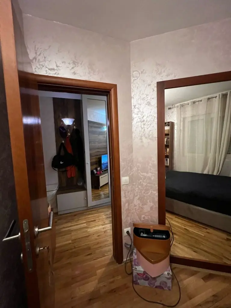 Hallway with two doorways, mirror, and bed in bedroom