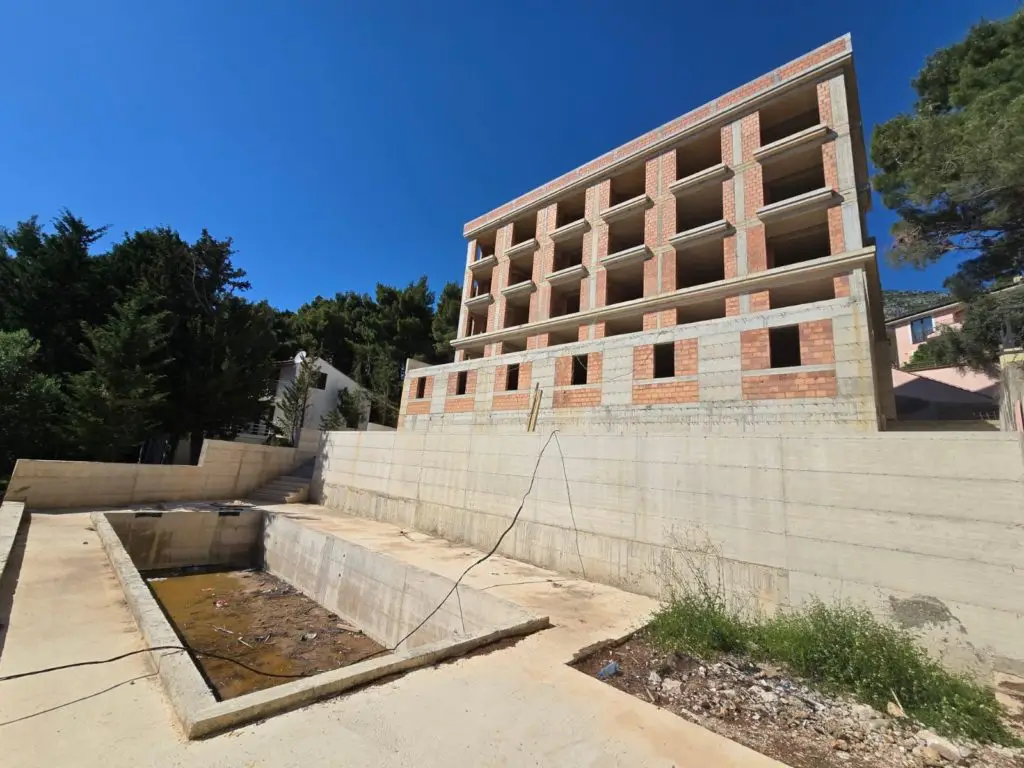 Unfinished brick apartment building above a concrete pool basin