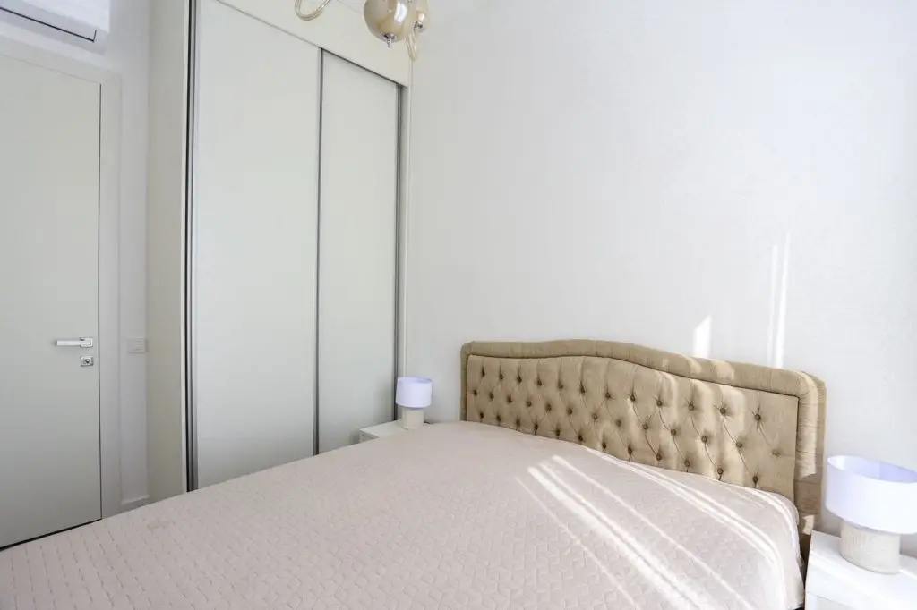 Bright bedroom with beige tufted headboard and white wardrobe