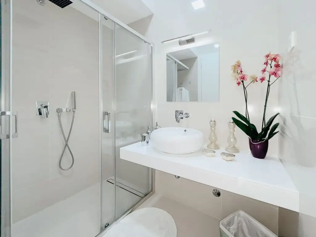 Modern white bathroom with glass shower, vessel sink, and orchid plant