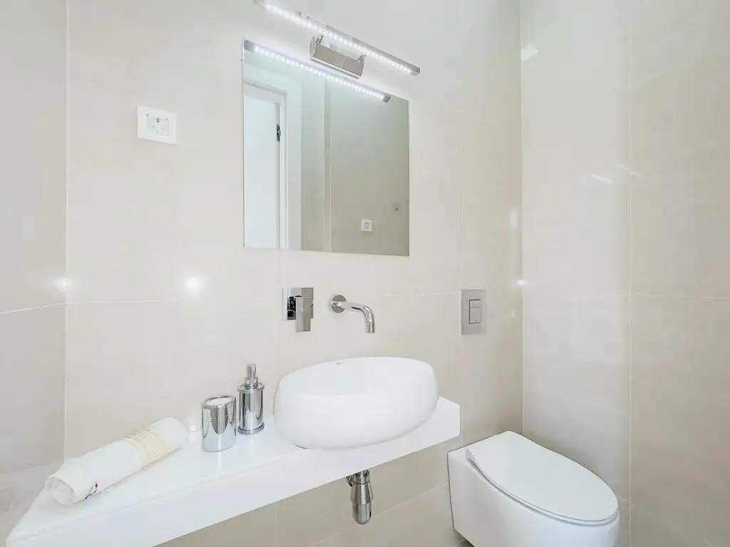 Modern beige bathroom with wall-mounted sink, mirror, and toilet