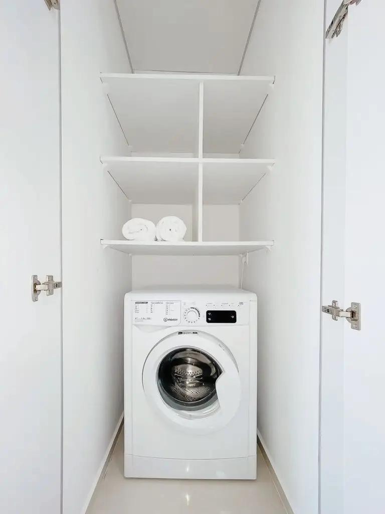 White front-loading washing machine in a closet with shelves and towels