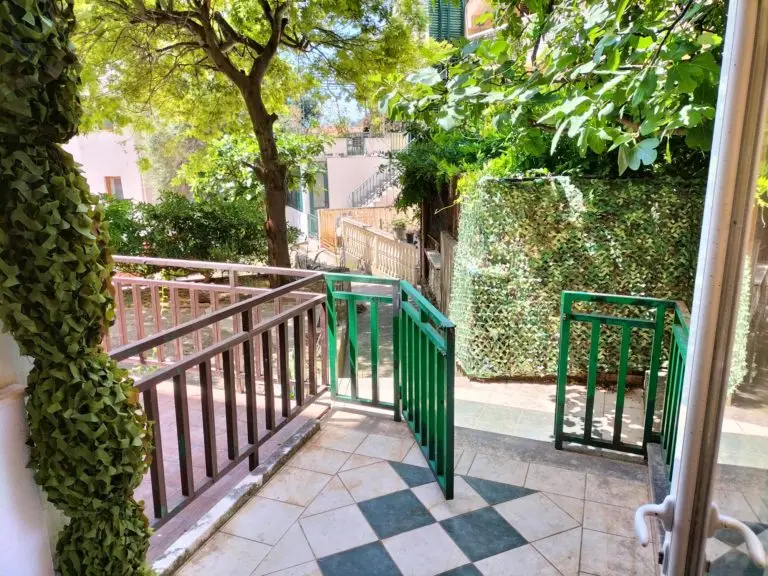 Tiled terrace with green railing and leafy courtyard view