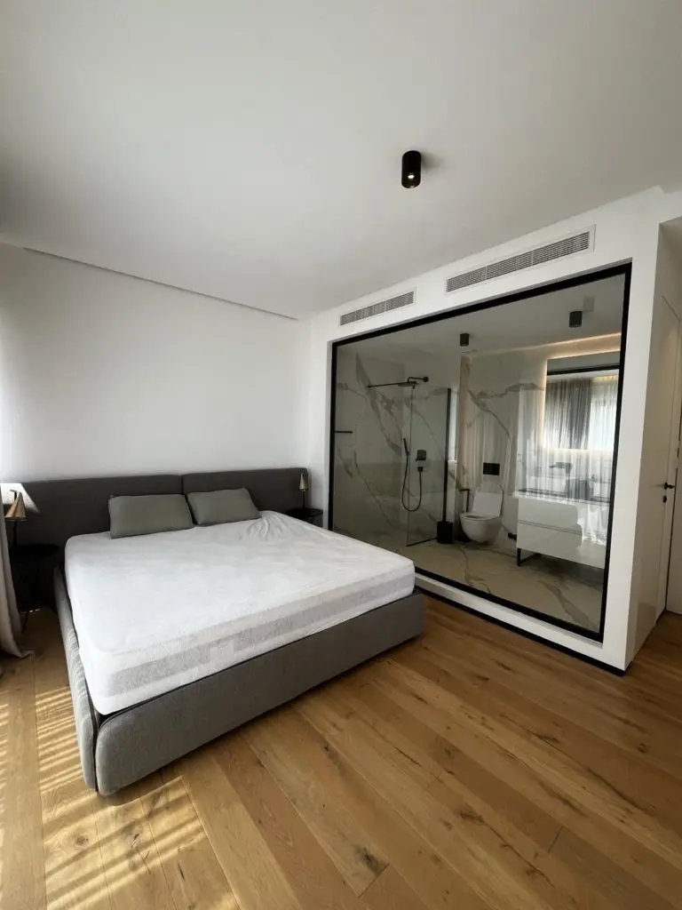 Modern bedroom with gray bed and glass-walled bathroom