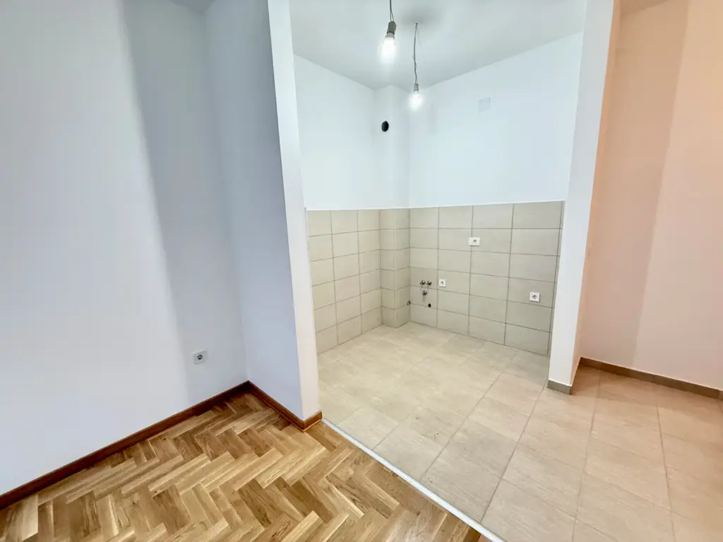 Empty apartment room with tiled kitchenette and wood floor