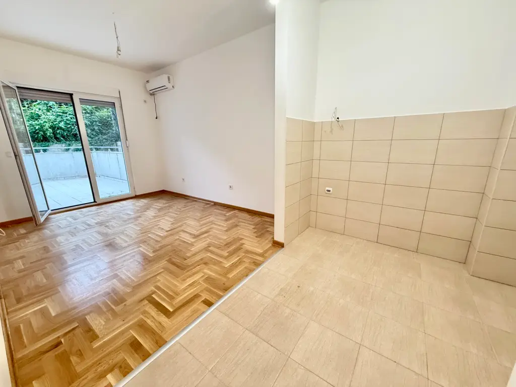 Empty apartment room with parquet floor and tiled kitchen area