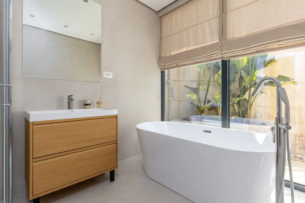 Modern bathroom with wood vanity and freestanding tub by window