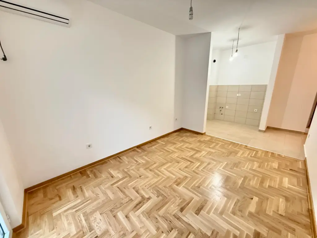 Empty room with herringbone wood floor and tiled kitchen area