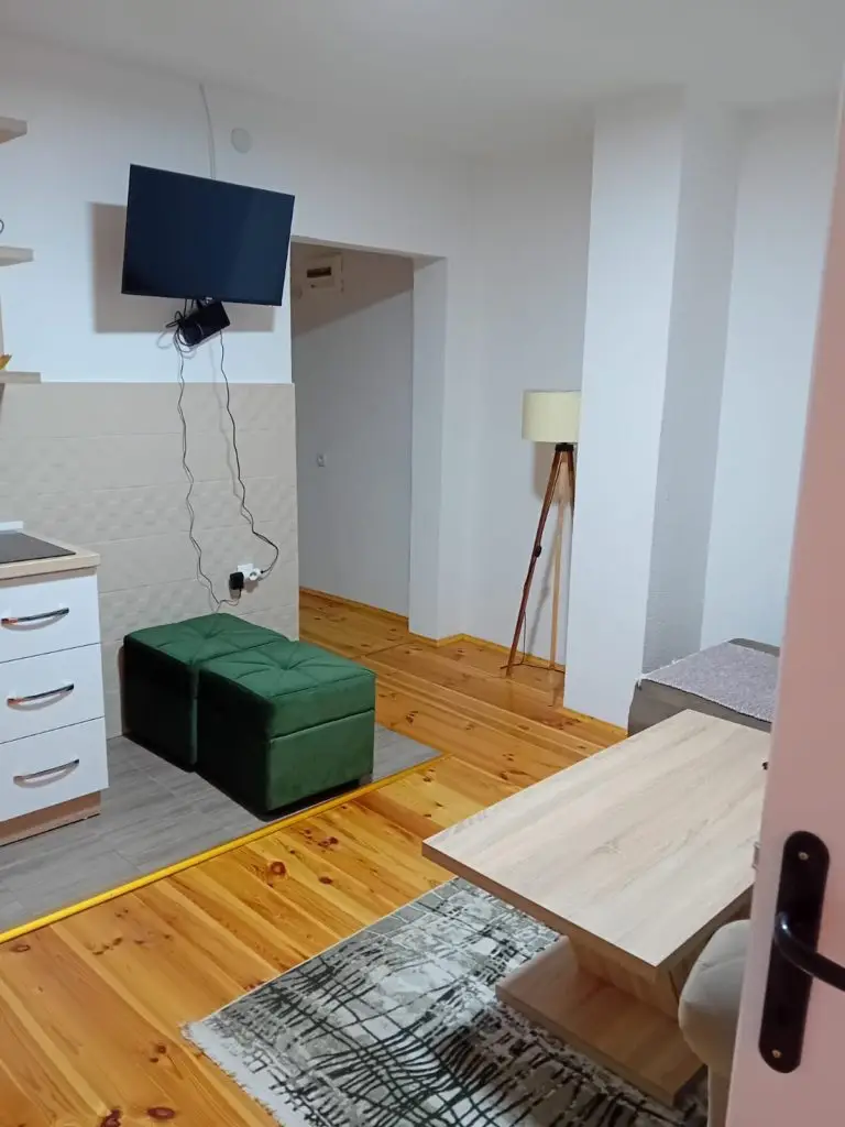 Small modern room with TV, green ottoman, and wooden floor