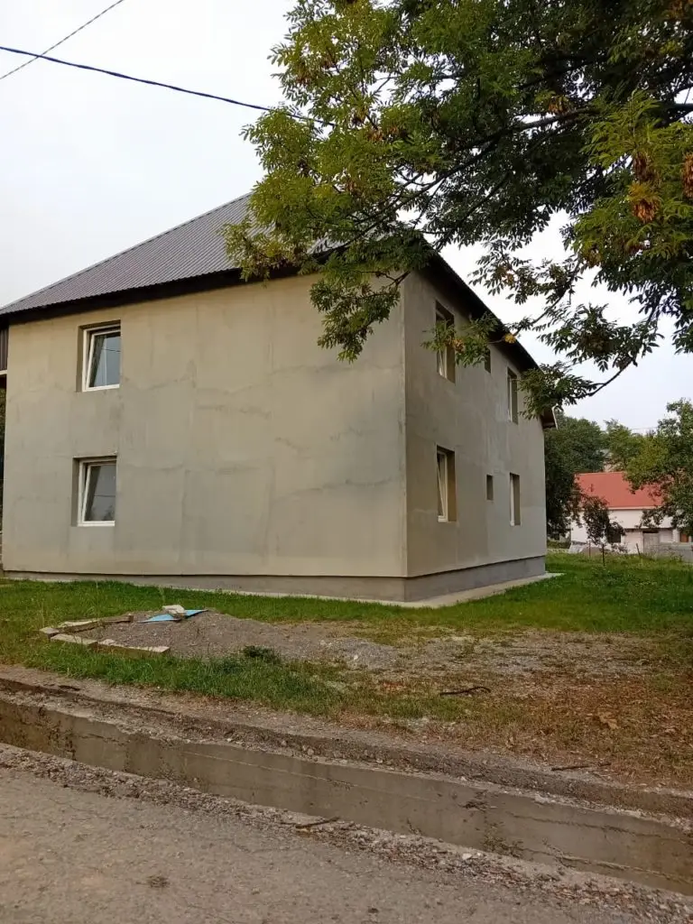 Unfinished gray two-story house with dark roof and yard