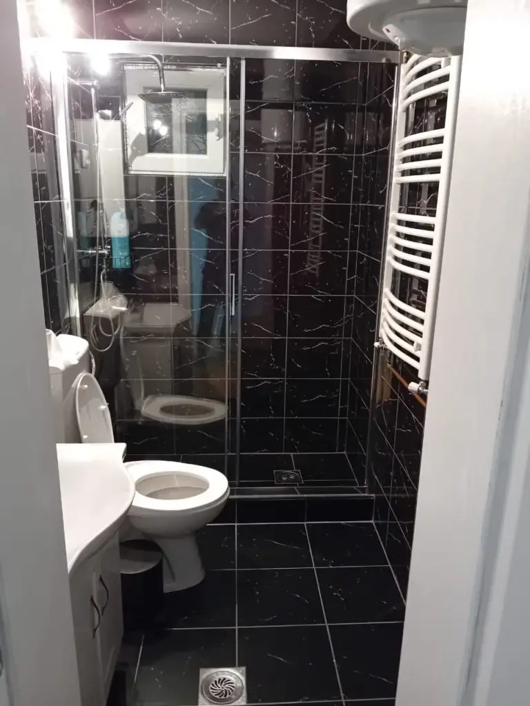 Black-tiled bathroom with shower, toilet, sink, and towel radiator