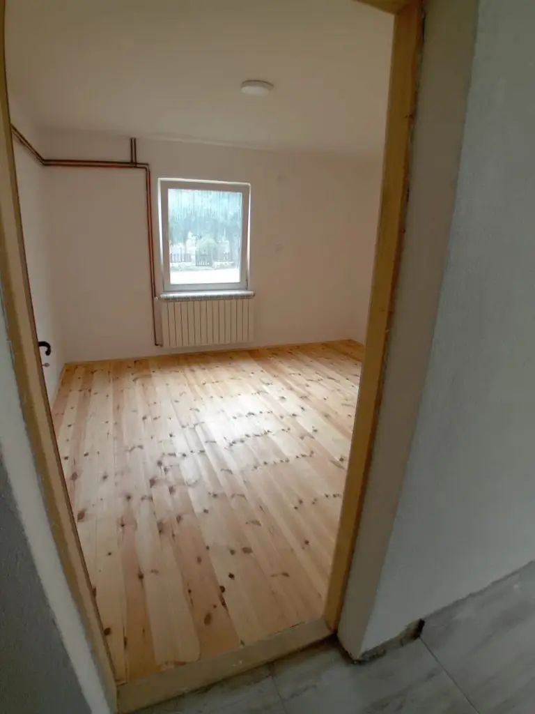 Empty room with wooden floor, window, and radiator