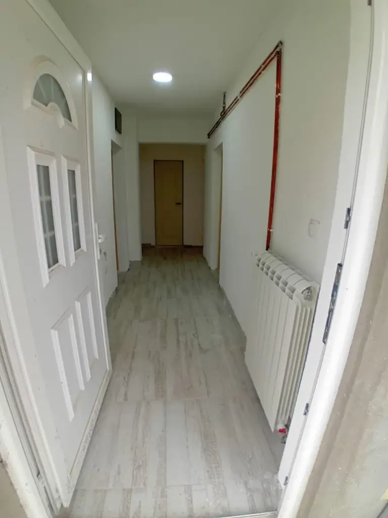 Narrow white hallway with radiator and wooden floor